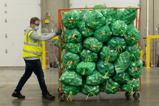 Person pulling a rack of filled BottleDrop Green Bags that are on their way to be processed.