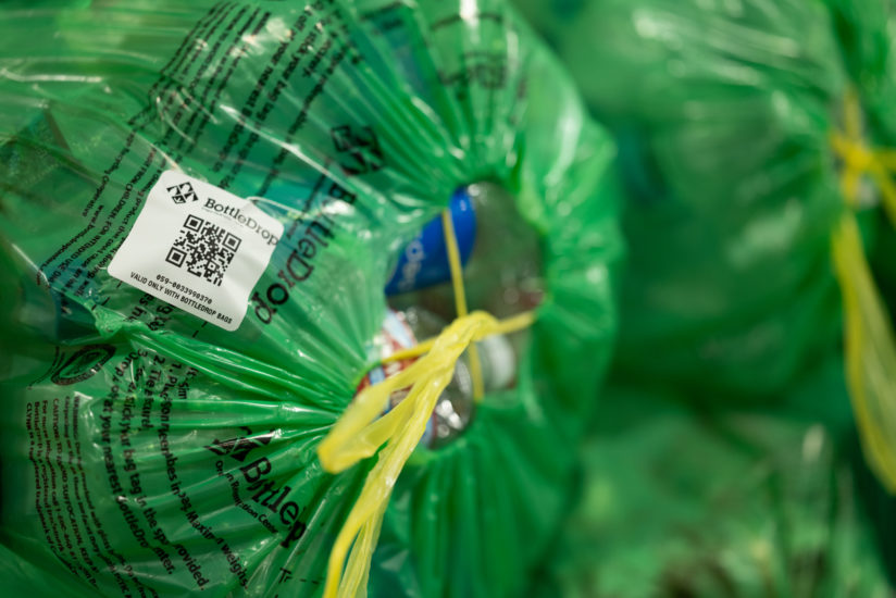 Close up image of a filled BottleDrop Green Bag that is cinched tightly and has a bag tag sticker that identifies it to a specific customer's account.